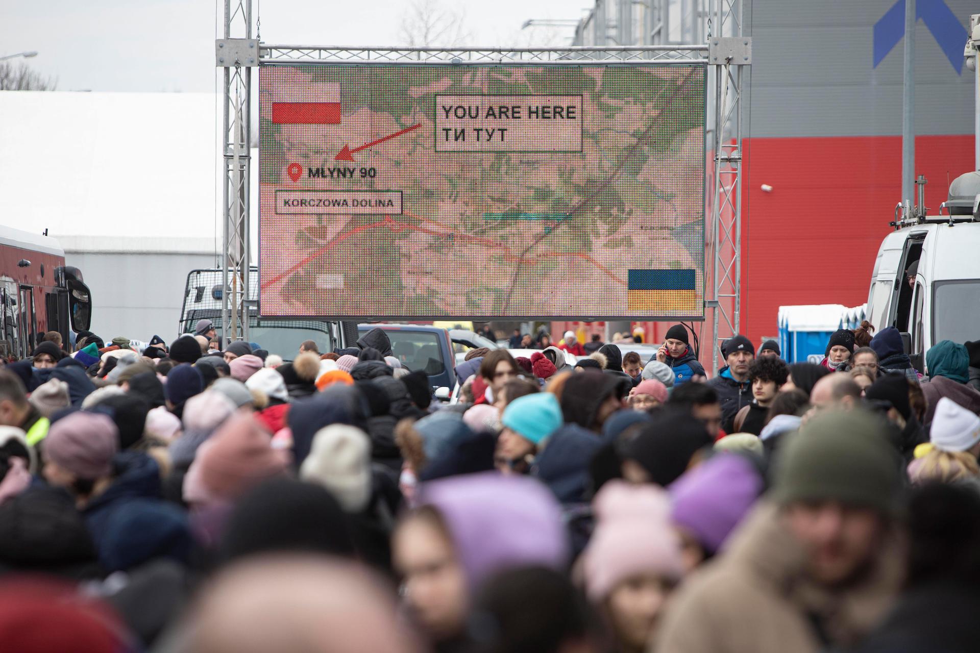 Swarms of people depicted at a train station as Ukrainian refugees arrive in Poland in March 2022. A large map reads: You are here.