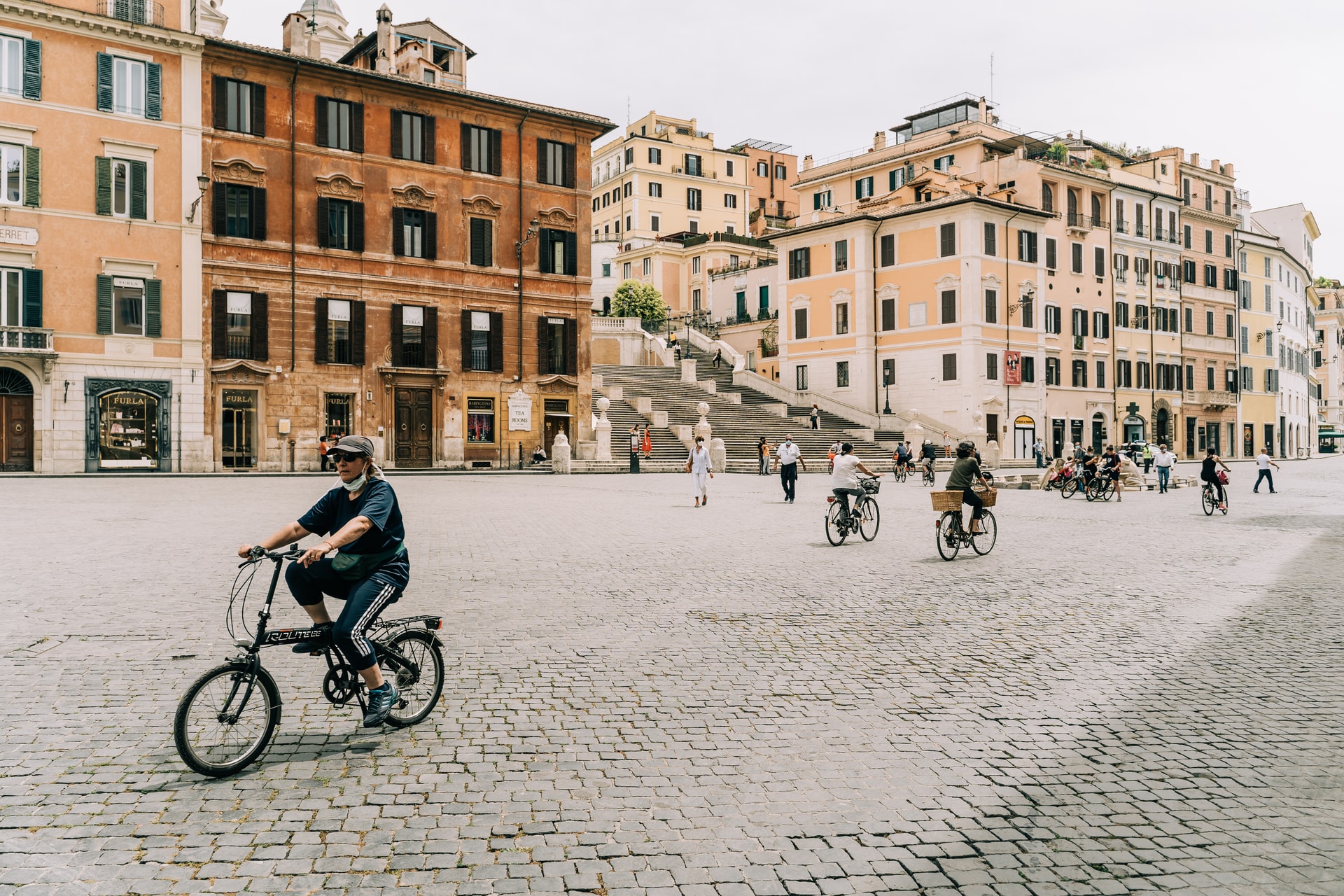 Image description: A wide cobbled street lined with historic four-and-five story buildings, painted in pastel shades of cream; the street is filled with cyclists. End of alt text.