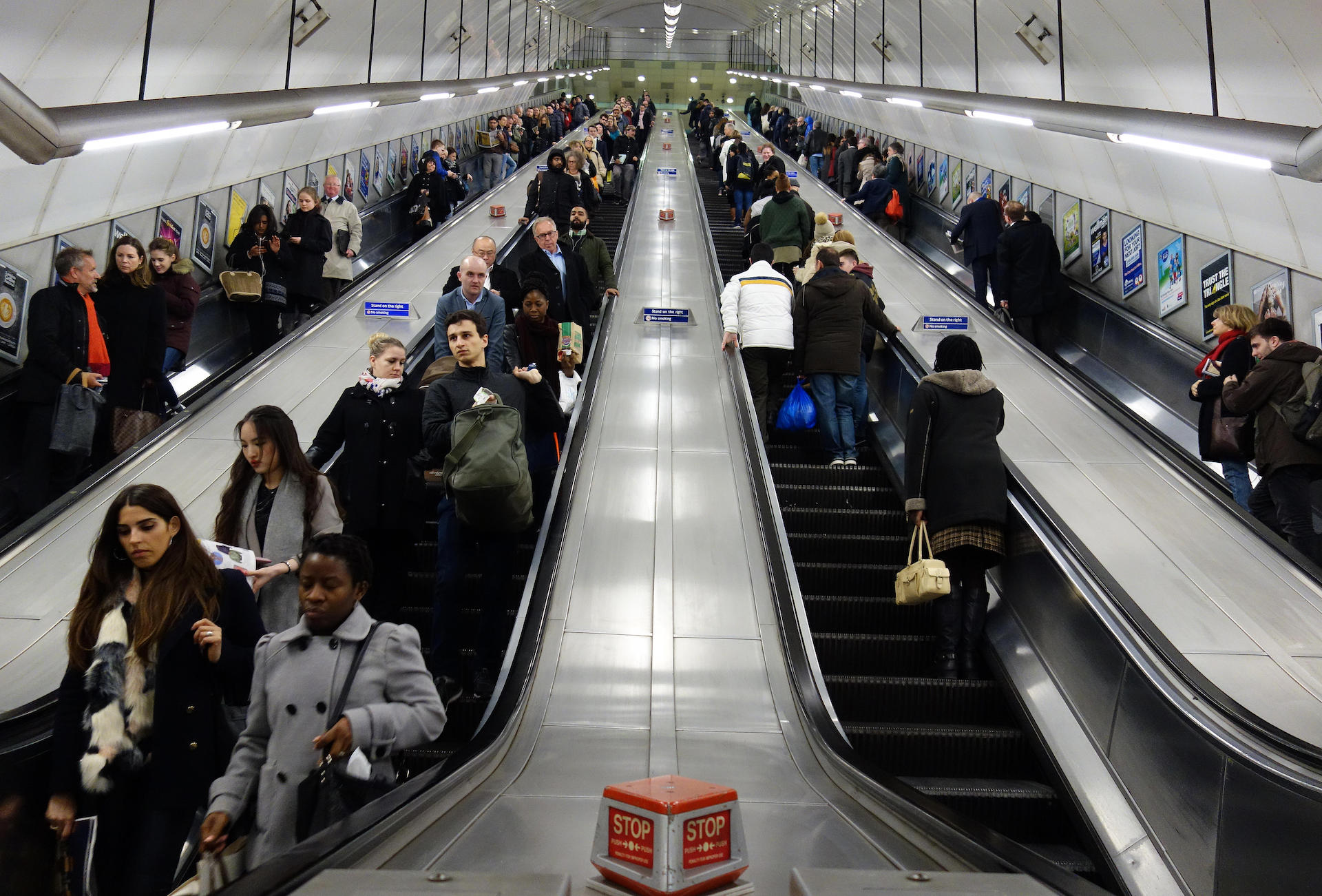 A photo taken from the bottom of four escalators, all filled with people, looking up towards the top exit. 